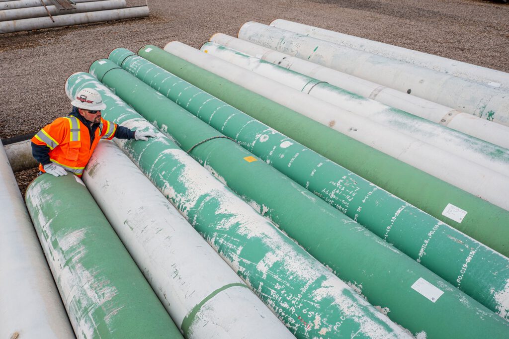 Pipes laying on ground with man in photo wearing safety vest.