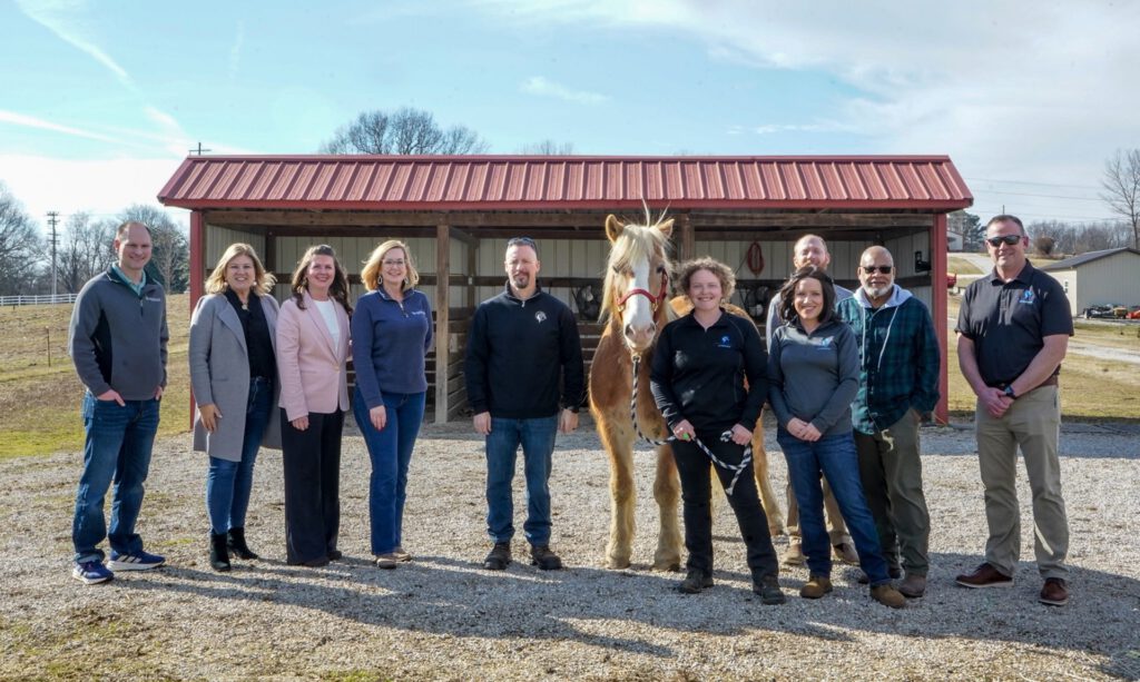 Southern Star Cares and Dream Riders team members pose for a group photo with the horse Tater Tot in front of a barn.
